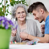 Seniorin spielt mit Pflegepersonal ein Brettspiel