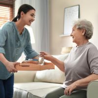 Young woman serving dinner for elderly woman in living room. Senior people care